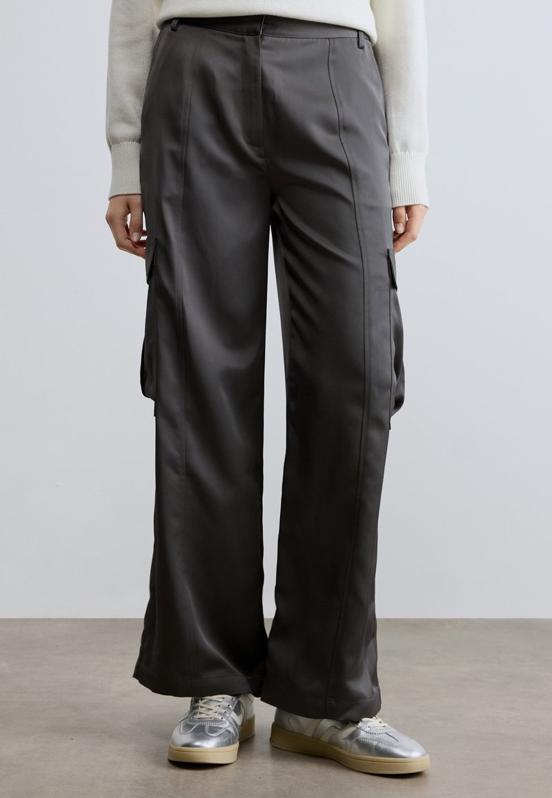 Sivé saténové cargo nohavice voľného strihu s bočnými vreckami a hladkou textúrou. Kombinované so striebornými teniskami a krémovým svetrom.