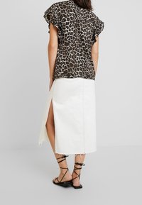 Blouse à imprimé léopard avec manches courtes à volants, associée à une jupe en denim blanc taille haute avec une fente latérale, et des sandales noires à lanières.