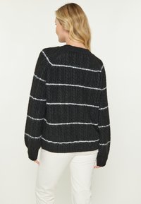 Pulover negru tricotat cu dungi verticale texturate și linii orizontale albe. Dispune de guler rotund și mâneci lungi.