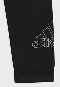 Musta urheiluhousut joissa on ribbireunus, ja joissa on näkyvä valkoinen Adidas-logo sekä kankaan sileä pinta.