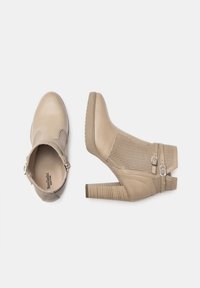 Bottines beiges en cuir lisse avec des panneaux perforés, dotées d'un talon carré et de deux boucles métalliques sur le côté.