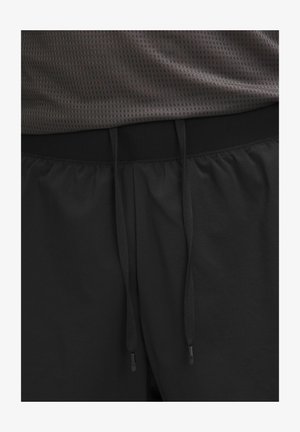 Crne sportske kratke hlače s elastičnim pojasom, opremljene podesivim vezicama. Materijal izgleda mekan i ima glatku teksturu.