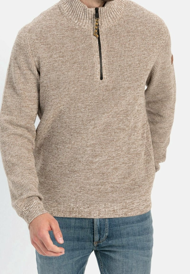 Beige gestrickter Pullover mit einem halben Reißverschluss, strukturiertem Stoff und gerippten Bündchen. Über blauen Denim-Jeans getragen, was ein lässiges Design zeigt.