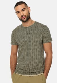 Kortærmet, fitted t-shirt i et grønt og cremefarvet geometrisk mønster med rund halsudskæring og glat bomuldsstof. Flade sømme og ingen synlige etiketter.