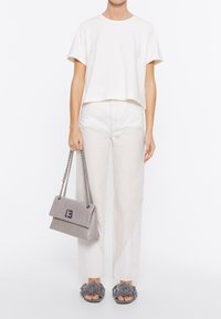 Maglietta bianca corta, jeans beige a vita alta con pannello a contrasto, borsa in pelle grigia e sandali scivolati grigi con motivo floreale.