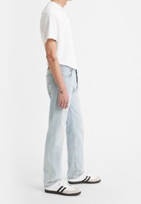 Unos vaqueros de denim azul claro con corte recto, combinados con una camiseta blanca básica y zapatillas blancas con rayas negras.