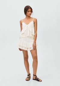Cream tiered dress with spaghetti straps, featuring ruffled layers and delicate lace trim. Paired with black strappy sandals.