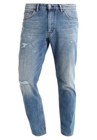 Jeans de denim azul claro con corte recto, que presentan una textura desgastada, un ligero desvanecimiento y parches visibles en la parte frontal.