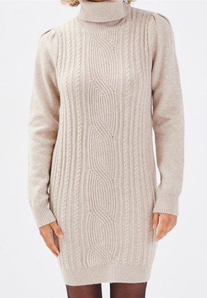 Vestito a collo alto in maglia cable beige con maniche allungate e polsini a coste. Il motivo testurizzato si sviluppa verticalmente lungo il centro.
