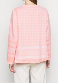 Jasnoróżowa bluzka z długim rękawem, ozdobiona wzorem w psa z houndstooth, teksturowanymi paskami oraz okrągłym dekoltem, o luźnym kroju i zaokrąglonym dole.