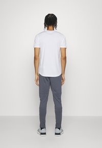 Balti trumpomis rankovėmis marškinėliai ir pilkos siaurėjančios sportinės kelnės, pasižyminčios glotnia tekstūra ir laisvu prigludimu. Komplektas užbaigtas juodais ir pilkais sportiniais batais.