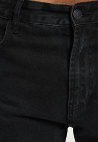 Black denim jeans featuring a classic five-pocket design, a button closure, and subtle textured fabric, with a slim fit and dark hue.