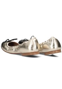Metallieke gouden balletschoenen met zwarte neuscaps, voorzien van een zachte leren textuur, elastische randen en zwarte satijnen strikjes aan de voorkant.
