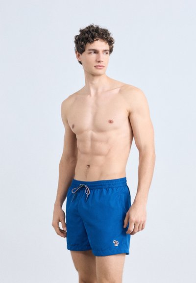 Shorts de bain bleus en tissu léger. Ils comportent une taille élastique avec un cordon de serrage et une petite étiquette-logo sur la cuisse gauche.