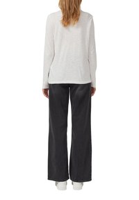 Haut blanc à manches longues avec une coupe décontractée, assorti à un jean noir taille haute à jambe large. La tenue est complétée par des baskets blanches.