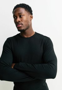 Fekete hosszú ujjú póló kerek nyakkivágással, sima anyagból készült, testhezálló ujjakkal, látható minták vagy grafikák nélkül.