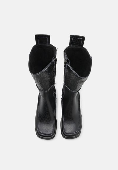 Botas de tornozelo em couro preto com acabamento texturizado, costura branca em contraste e fechos de correr laterais. Apresentam uma ponta retangular e sola robusta.