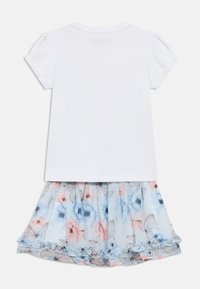 Λευκό πουκάμισο με κοντά μανίκια και φουσκωτά μανίκια με πιέτες, συνδυασμένο με φούστα σε ανοιχτό μπλε χρώμα που έχει σχέδια με λουλούδια και πεταλούδες, και βολάν στο τελείωμα.