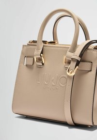 Sac à main en cuir texturé beige avec poignées doubles, quincaillerie dorée, logo embossé, bandoulière amovible et fermeture à glissière.