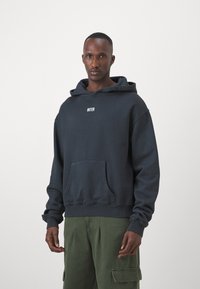 Sweatshirt com capuz azul-marinho, apresentando um bolso frontal e texto branco "INTER". Estilizado com calças cargo verdes, mostrando mangas longas e um corte descontraído.