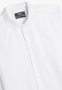 Chemise blanche à manches longues, coupe regular, en tissu lisse. Dotée d'un col classique et de six boutons blancs sur le devant.