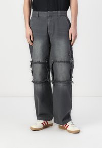 Gray baggy cargo pants with frayed details, side pockets, and a worn fabric texture; paired with white shoes featuring red stripes.