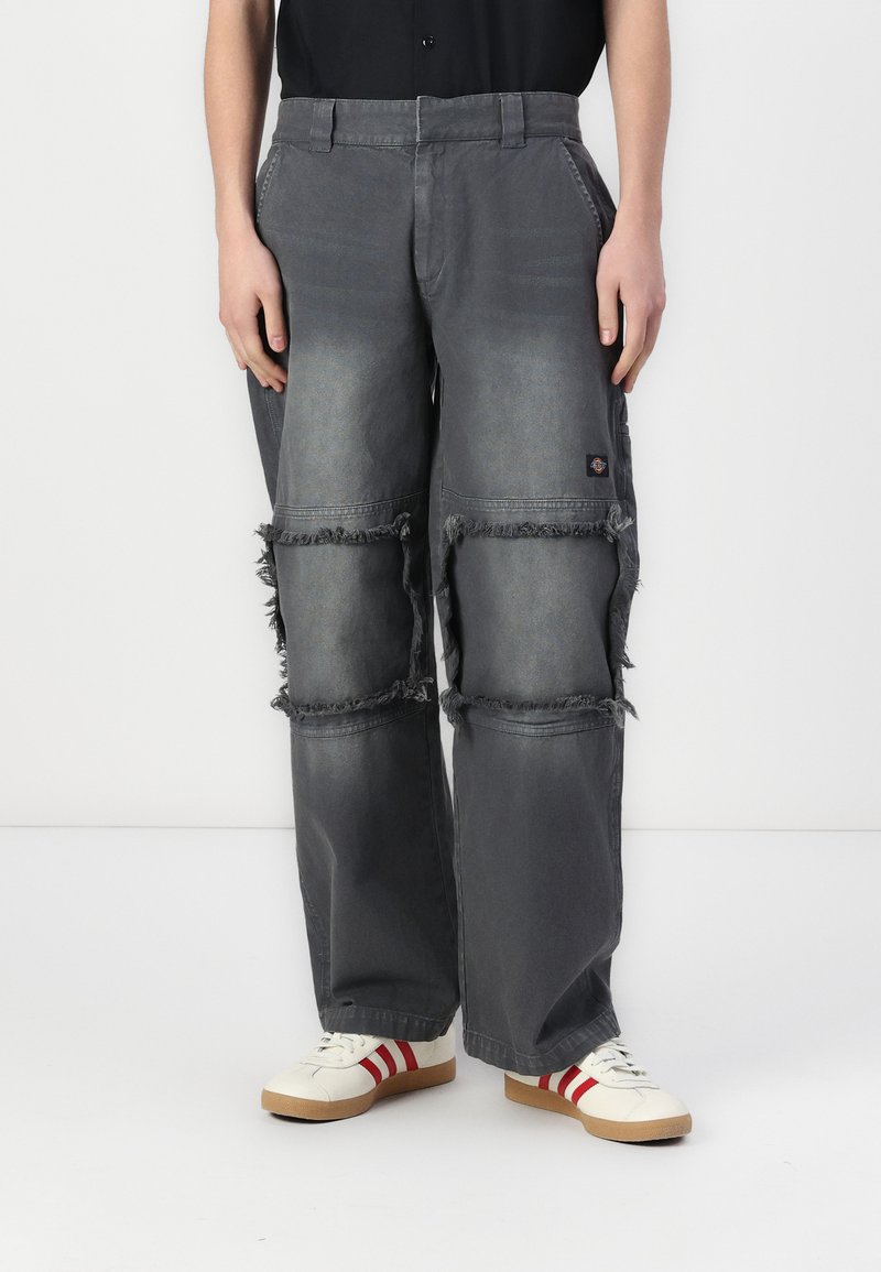 Gray baggy cargo pants with frayed details, side pockets, and a worn fabric texture; paired with white shoes featuring red stripes.