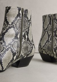 Cizme scurte din piele cu imprimeu de șarpe în nuanțe de negru și crem, cu fermoar lateral și toc pătrat. Pielea texturată adaugă un plus de interes vizual.