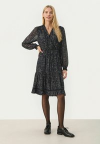 Rochie neagră, cu mâneci lungi din material transparent, având un model de puncte metalice aurii și un tiv cu volane în straturi. Stilizată cu pantofi negri și colanți.