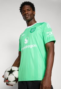 Zöld focimez fehér részletekkel, melyen a "Snapdragon" logó és felirat látható. A játékos egy fekete-fehér mintás focilabdát tart.