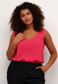 V-neck sleeveless top in bright pink fabric, with a relaxed fit and a slight sheen, paired with black high-waisted trousers.