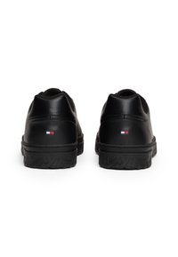 Baskets en cuir noir avec une semelle en caoutchouc texturé, arborant un petit logo coloré au niveau du talon et un design lisse et arrondi.