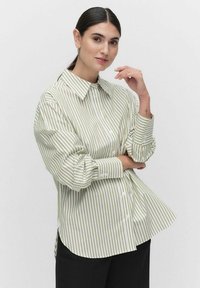 Light green and white striped oversized shirt with a button-up front, long sleeves, and a pointed collar, made of smooth fabric.