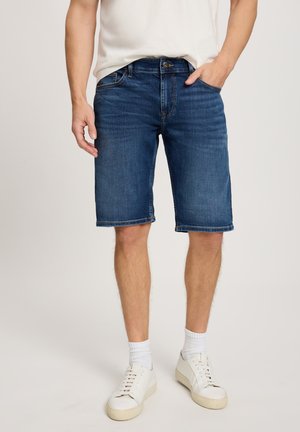 Jeansowe szorty w ciemnoniebieskim kolorze, z klasycznym pięciopocketowym krojem, stworzonym z przeszyciami i prostym fasonem. Połączone z białymi trampkami i skarpetkami.