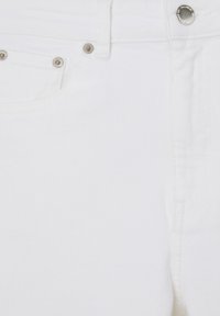 Gros plan sur un jean en denim blanc montrant la poche avant, le bouton argenté et les rivets sur la ceinture et le bord de la poche.