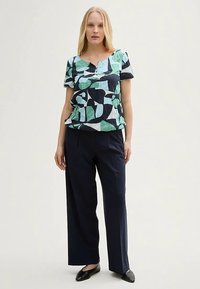 Floral patterned short-sleeve top in blue, green, and white, paired with navy wide-leg trousers. Material appears lightweight and textured.