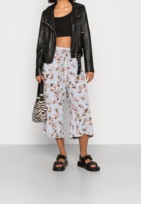 Black leather biker jacket, black cropped top, light blue floral wide-leg pants, and chunky black platform sandals with buckles. Zebra-print bag.