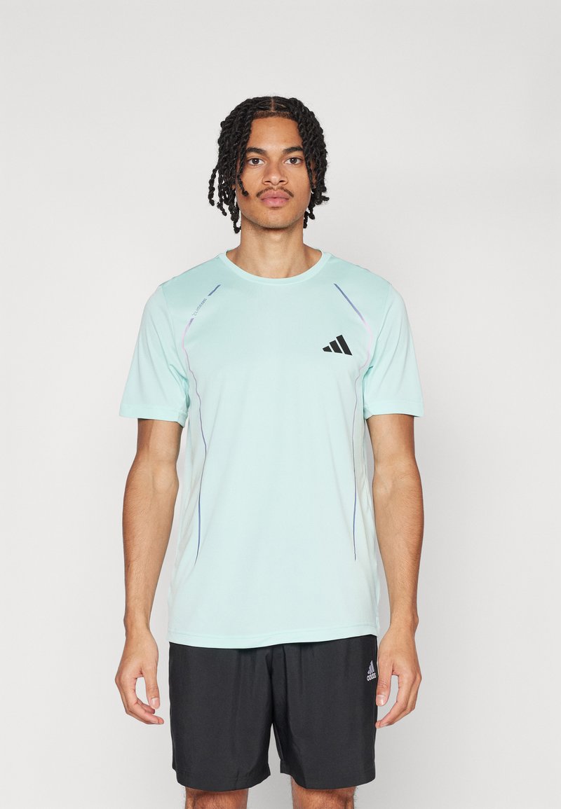 Lyseblå treningst-skjorte med korte ermer, rund hals, svart Adidas-logo og subtile lilla aksentlinjer. Brukt med svarte shorts.