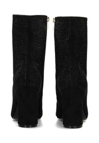 Bottines noires en daim avec une surface texturée ornée de petits clous métalliques. Talon épais et zips sur les côtés pour la fermeture.