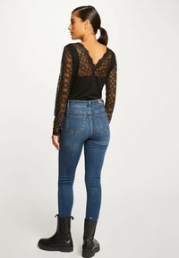 Top nero a maniche lunghe con maniche in pizzo e scollo a ondine, abbinato a jeans skinny blu a vita alta e stivaletti neri.