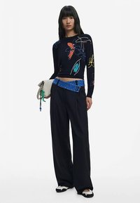 Czarna bluzka z długim rękawem w kwiatowe wzory w kolorach czerwonym, niebieskim i żółtym, w połączeniu z luźnymi czarnymi spodniami i paskiem z niebieskim akcentem.