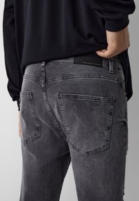 Gray denim jeans with a distressed finish, featuring two back pockets and a black leather label with embossed text near the waistband.