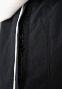 Gros plan sur une fermeture éclair noire sur un tissu noir avec un bord blanc partiellement dézippé, mettant en évidence les détails de texture et de couture.