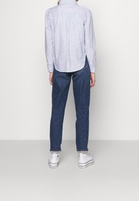 Camicia azzurra chiara a maniche lunghe con un motivo a trama, pieghe posteriori e spacchi laterali, abbinata a pantaloni in denim blu scuro e sneaker bianche.