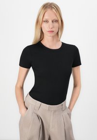 Sort ribbet T-shirt med korte ærmer og rund halsudskæring, parret med lys beige højtaljede bukser med sidelommer og folder.