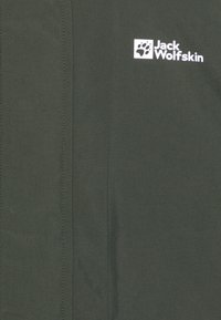 Tume roheline jakk sileda tekstuuriga, millel on valge logo vasakus ülanurgas. Šeemi detailsed jooned kulgevad vertikaalselt mööda kangast.