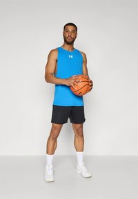 Kék sport trikó, fekete rövidnadrág és fehér sportcipő. A modell narancssárga kosárlabdát tart, semleges háttér előtt áll.