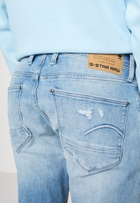 Ljusblå denimjeans med en sliten textur, med två bakfickor och G-Star Raw-logotyp över midjan.