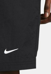 Black Nike shorts with a smooth texture. Features a white logo near the hem, short length, and a straight cut design.