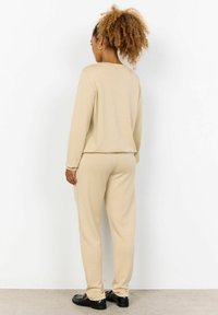 Helles beige Lounge-Set bestehend aus einem langärmeligen Oberteil und schmal zulaufenden Hosen, gefertigt aus weichem Stoff mit lockerem Schnitt und minimalen Nähten.